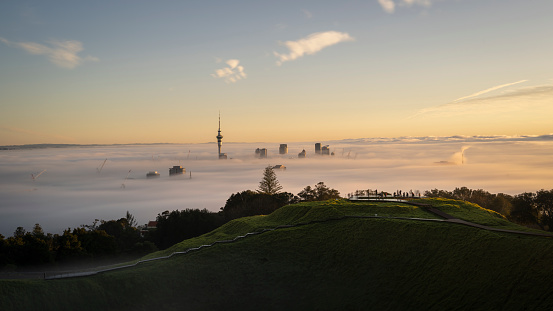 Sky Tower and Auckland city in the fog at sunrise, from Mount Eden summit.
