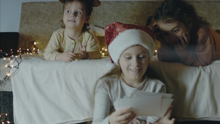 Three little girls looking together at old pictures on a Christmas night. Christmas lights around. Christmas and bonding concept.