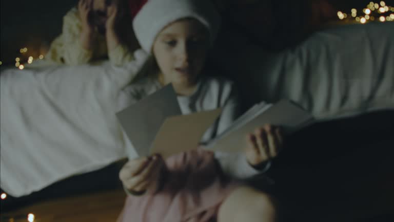 Three little girls looking together at old pictures on a Christmas night. Christmas lights around. Christmas and bonding concept. Handheld shooting