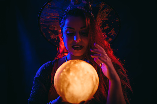 Beautiful young plus size woman dressed like a witch holding a crystal ball under neon lights.
