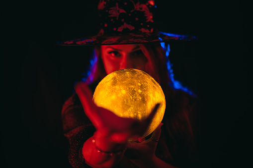 Portrait of a beautiful young plus size woman dressed like a witch holding a crystal ball under neon lights.
