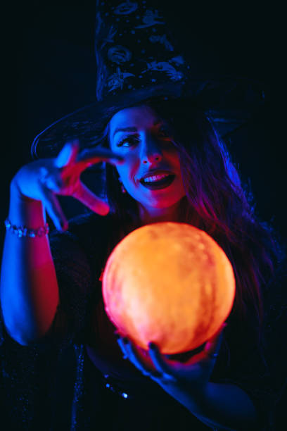 young woman dressed like a witch holding a crystal ball - fortune telling paranormal neon light prophet imagens e fotografias de stock