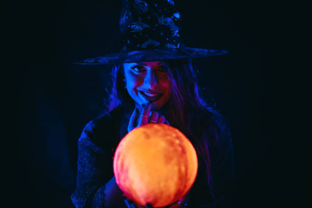 young woman dressed like a witch holding a crystal ball - fortune telling paranormal neon light prophet imagens e fotografias de stock