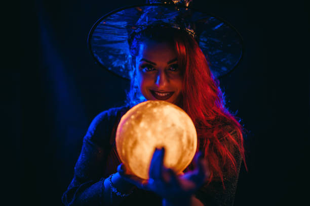 young woman dressed like a witch holding a crystal ball - fortune telling paranormal neon light prophet imagens e fotografias de stock