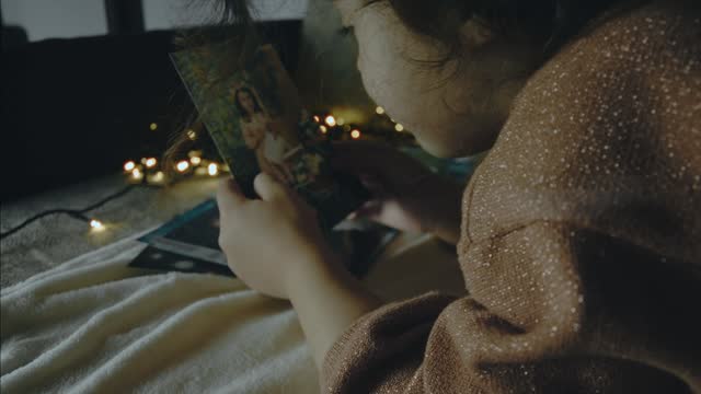 Little girl looking at old pictures on a Christmas night. Christmas lights around. Christmas and leisure concept.