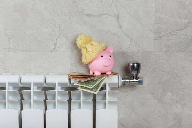 Savings concept.Money in piggy bank on radiator on a gray wall background. Concept of heating season. Concept of expensive heating costs and rising energy bill prices for winter cold season. concepto de ahorro. dinero en alcancía en radiador sobre fondo de pared gris. concepto de temporada de calefacción. concepto de costos de calefacción caros y aumento de los precios de las facturas de energía para la temporada de frío de invierno.