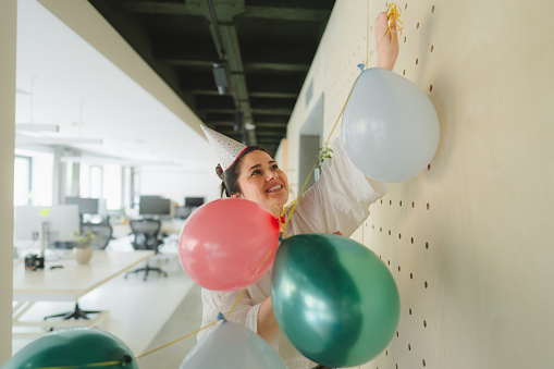 Photo of a young woman putting up the balloons and having the last preparations for the office party