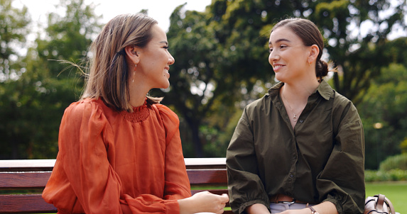 Friends, women and laughing at park on bench, bonding and talking together. Girls, outdoor and happiness of people in conversation, comic discussion or comedy and enjoying quality time for friendship