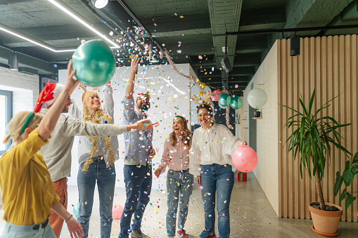 Photo of a group of coworkers having good time at a Christmas party in the office - partying, dancing, drinking and throwing confetti