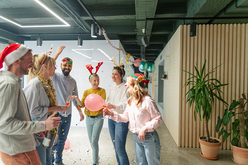 Photo of a group of coworkers having good time at a Christmas party in the office - partying, dancing, drinking and throwing confetti