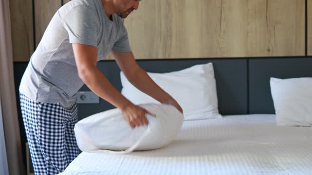 Close-up of a man putting a pillowcase on his pillow at home or in a hotel. Man Making the Bed