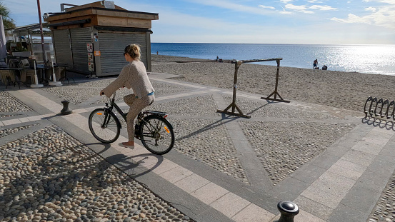 She is riding along a cobblestone promenade by the Mediterranean Sea, Liguria