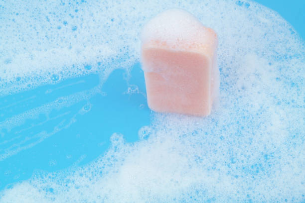 Pink sponge with foam on blue background. Washing and cleaning concept.