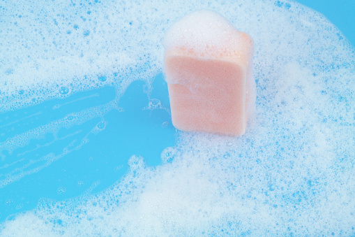 Pink sponge with foam on blue background. Washing and cleaning concept.