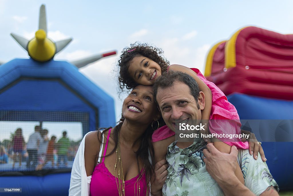 Young parents and child at a festival with inflatables Child and her parents posing for a group photo at a summer festival. Family Stock Photo