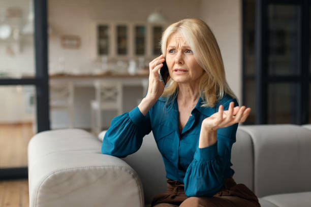 istock Stressed mature woman talking on cellphone, having unpleasant phone conversation while sitting on sofa at home 1766721463
