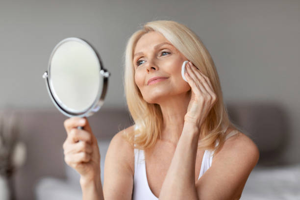 istock Beautiful middle aged lady looking in mirror, erasing make up from her face, using cotton pads and cleansing lotion 1766721935