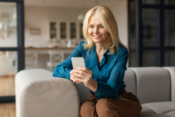 istock Smiling mature woman with smartphone sitting on couch, texting, browsing internet, purchasing in online web store 1766722013