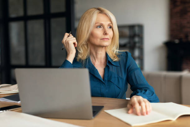 istock Serious pensive mature businesswoman with computer making notes, planning day, looking at free space, working at home 1766722093