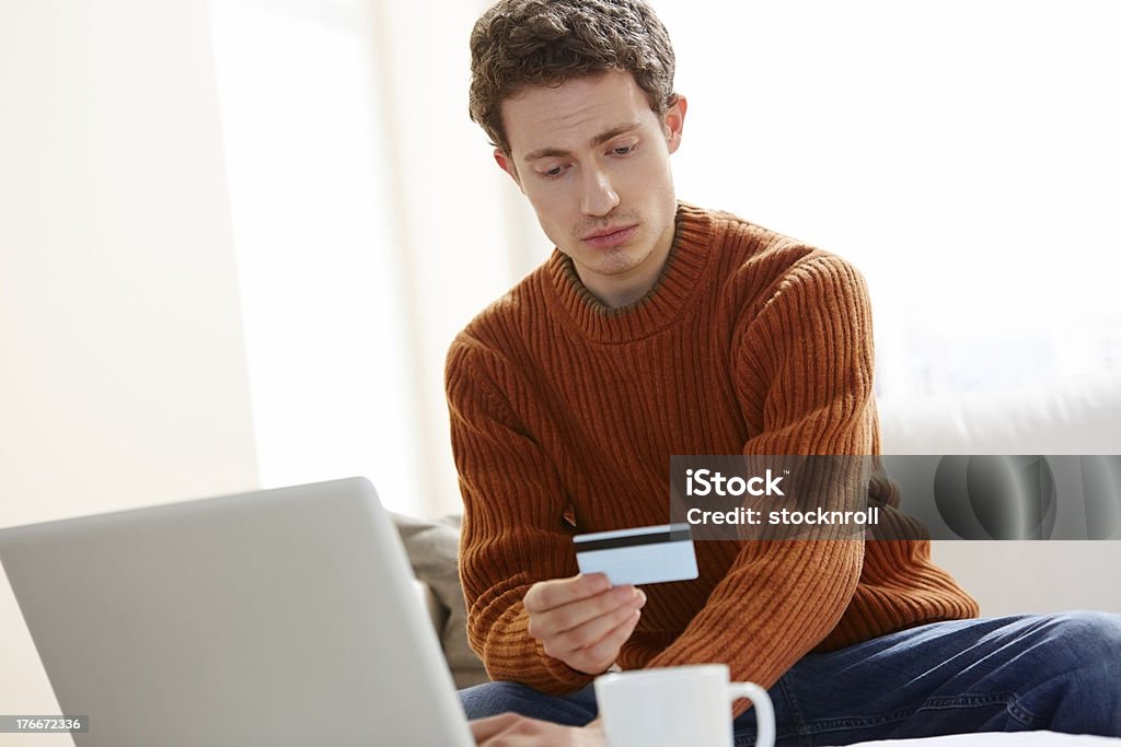 Young man making online payments with credit card Young man sitting at home making online payments with his credit card 20-24 Years Stock Photo