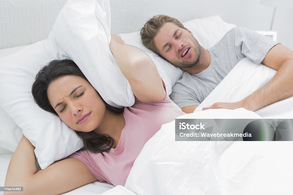 Mulher Cobrindo Orelhas com travesseiro enquanto o marido dorme - Foto de stock de Acordar royalty-free