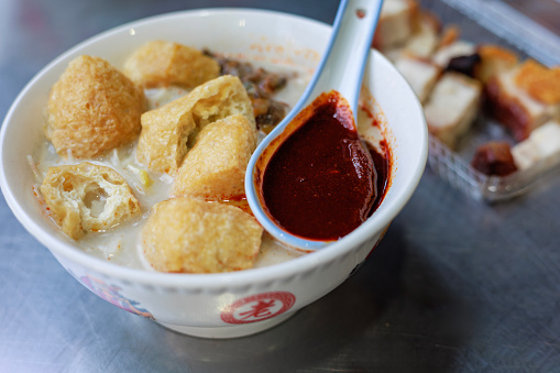 Penang's famous Curry Mee is a flavorful dish served with coagulated pig's blood, prawn, cuttlefish, cockles and topped with spicy chili paste.