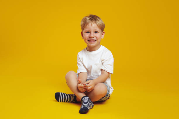 istock Cheerful kid smiling and looking at camera while sitting crossed legged on floor against yellow 1766767186