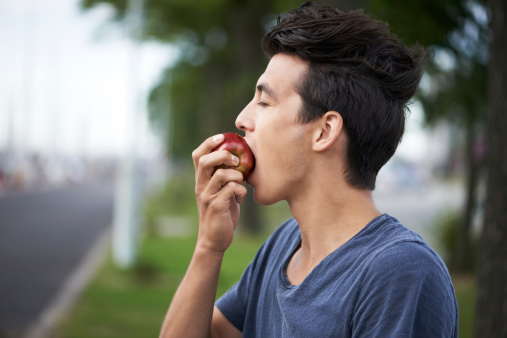 A young man taking a bite of an apple while waiting for the bus