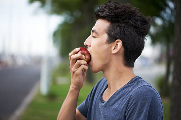 Taking a bite A young man taking a bite of an apple while waiting for the bus apple bite stock pictures, royalty-free photos & images