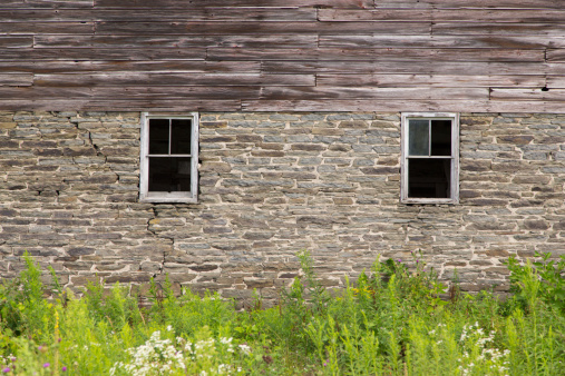 Two windows in the stone wall foundation of an old, gray barn.