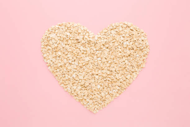 forme de coeur créée à partir d’avoine roulée sèche sur fond de table rose clair. couleur pastel. j’adore les aliments sains. closeup. vue de haut en bas. - oatmeal oat heart shape rolled oats photos et images de collection