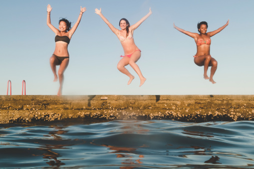 Three young women jumping into the sea during the summer.
