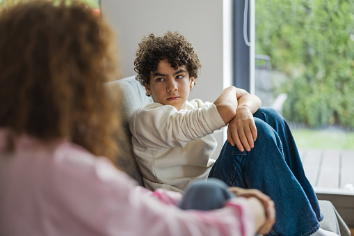 Upset boy sitting on sofa while his mother looking at him