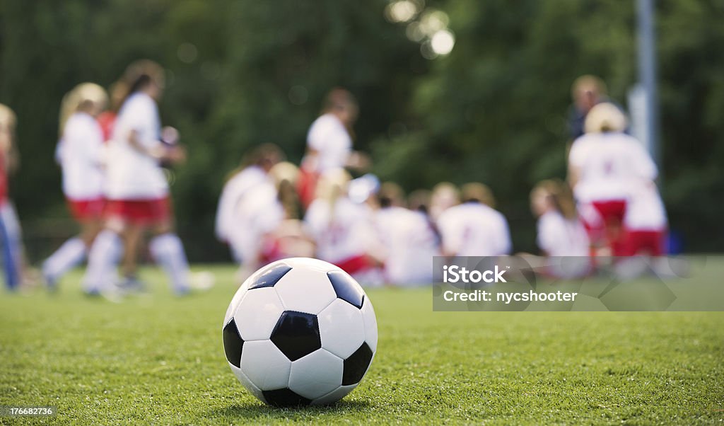 Close-up of a Soccer Ball in front of a Female Soccer Team Close-up of soccer ball with girls soccer team in the background listening to coach. Halftime Show Stock Photo