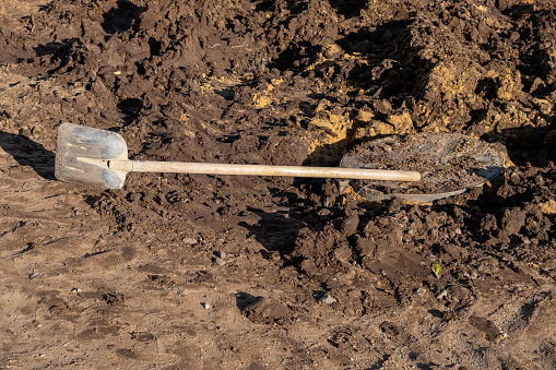 A shovel with a long wooden handle, a tool used for digging, lying on the soil. Concept of construction site, construction, digging earth.