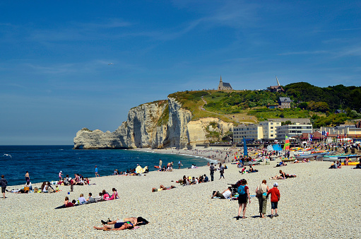 Etretat, France - June 02, 2011: Unidentified people enjoy a sunny day on beach with formation in Etretat, chapel and monument for Nungesser and Coli- two airmen who tried to cross the atlantic