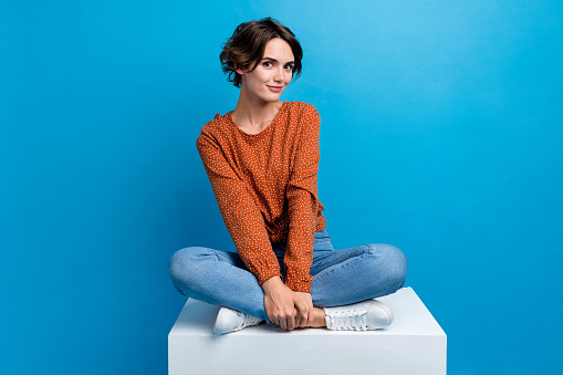 Full body photo of pretty young girl sit white platform model shopping wear trendy brown outfit isolated on blue color background.