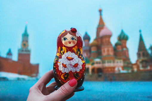 Russian doll, traditional toy Matryoshka on the background of the historical centre of Moscow: Kremlin, Saint Basil`s cathedral. Post card from Russia. Horizontal winter photo of travel souvenirs.