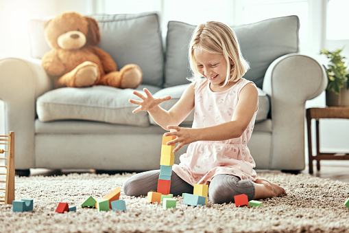 Kid, playing alone and toys on living room floor, house and educational game, fun and child development. Building blocks, girl and learning for creativity with activity, relax indoors and happiness