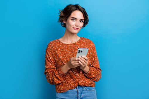 Photo portrait of attractive young woman hold device write comment dressed stylish brown clothes isolated on blue color background.