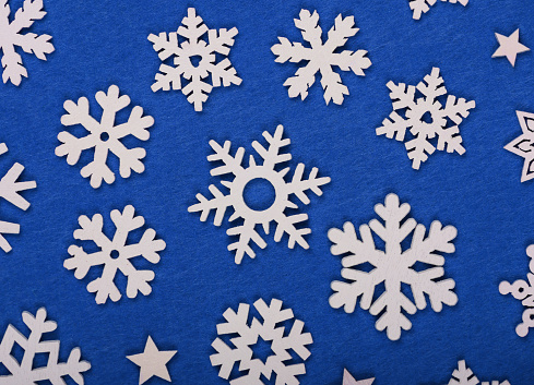 Close up pattern of white wooden snowflakes Christmas decoration over blue felt background, table top view, flat lay