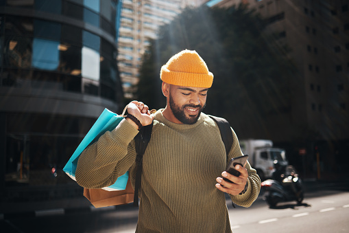 Student, phone and shopping bag in city travel, walking and search for student deal, discount or online sale. Happy african man with retail gift and mobile app, social media and chat in urban street