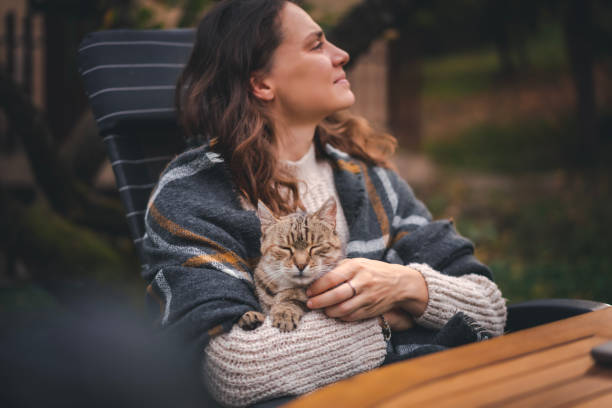 A young woman sitting in the autumn garden with a pet gray cat in her hands enjoys the fresh air stock photo