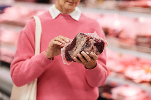 Closeup of adult woman holding fresh meat shopping for groceries in supermarket, copy space