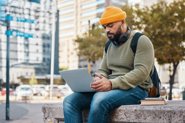istock Student, man and computer in city for college application, university research or scholarship website information. Happy african person on laptop, typing and studying philosophy or language on campus 1766905149