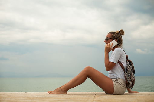 Young woman sitting on beach and using smart phone.