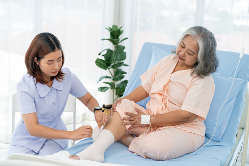 Elderly Asian patient admitted to hospital A nurse cares for a patient's injured leg bandage. A nurse takes care of patients in a hospital or clinic.