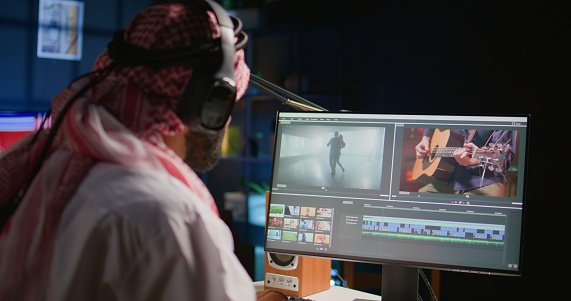 Middle Eastern content creator editing cinematographic project, creating film montage, working with images and sounds. Teleworking artist doing color grading on computer screen