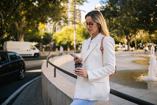Portrait of a beautiful, young business woman enjoying coffee and using mobile phone on the street.