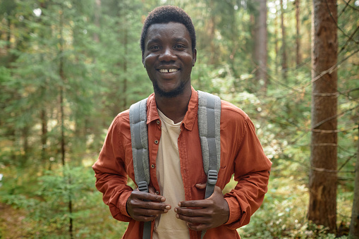 Portrait of African American hiker with backpack smiling at camera while travelling in the forest